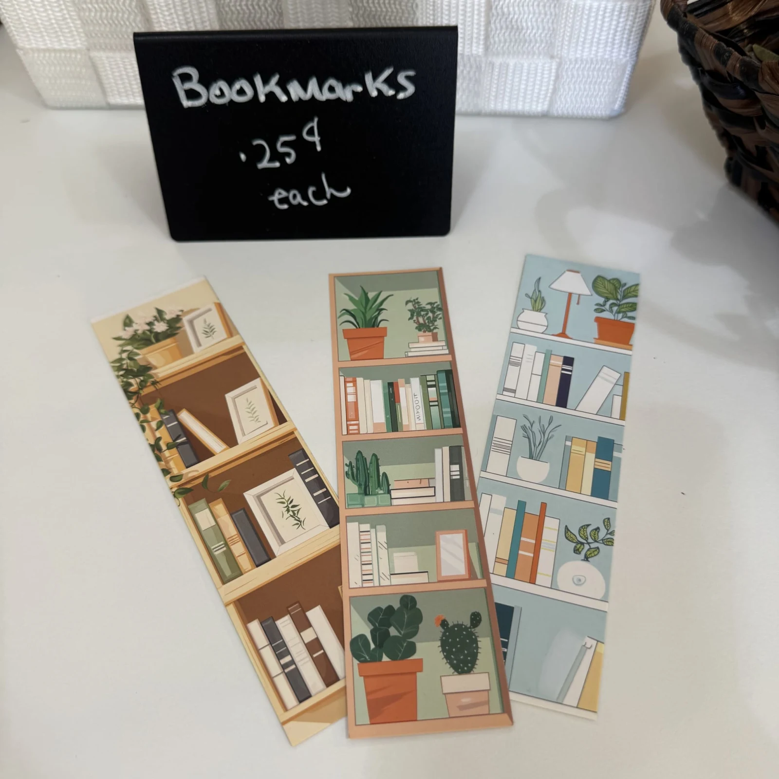 Three decorative bookmarks featuring illustrated bookshelves and potted plants, priced at 25 cents each.