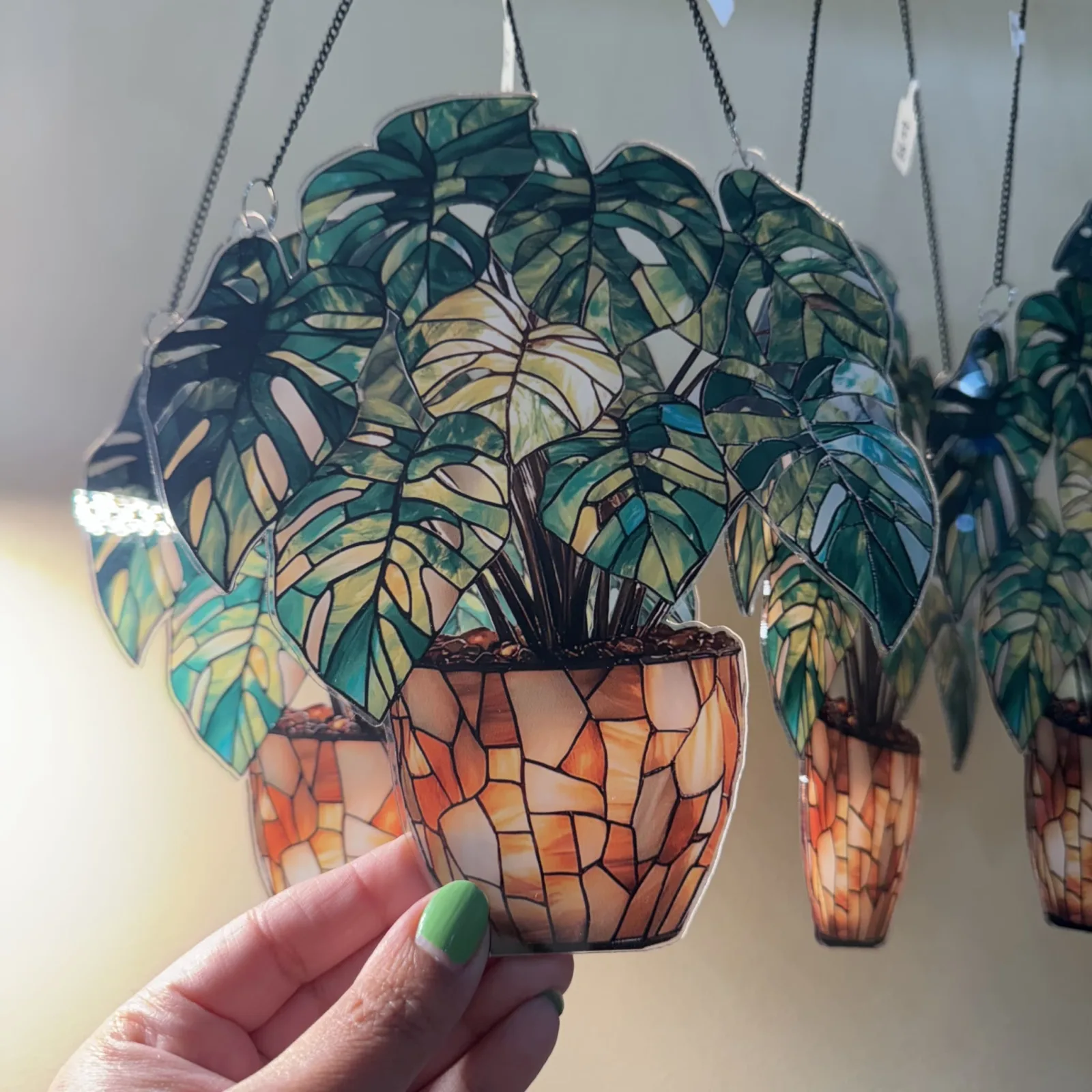 Monstera Suncatcher Acrylic hanging plant with mosaic pot, held in hand against sunlight.