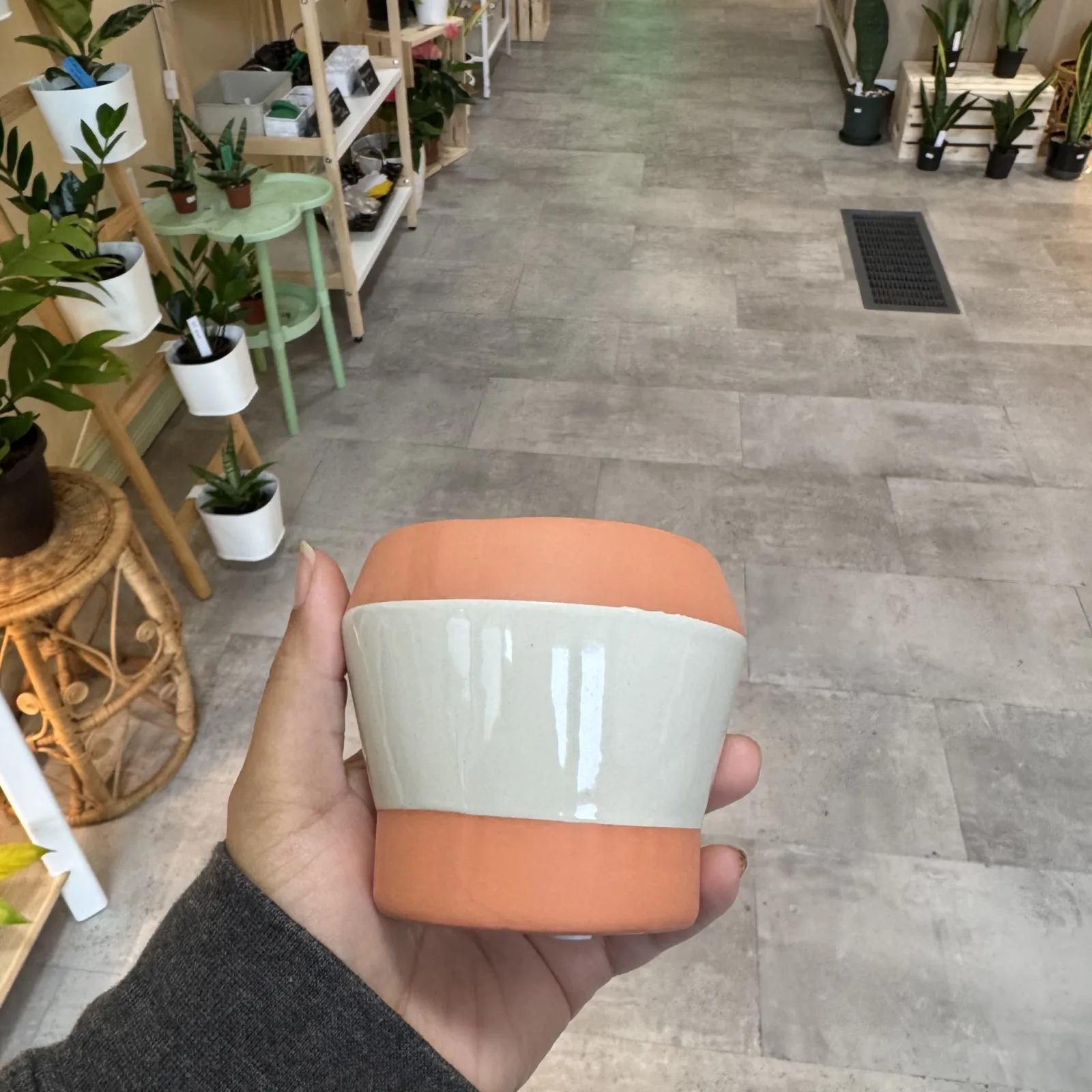 Peach and Taupe Pot held in hand in plant shop with greenery background.