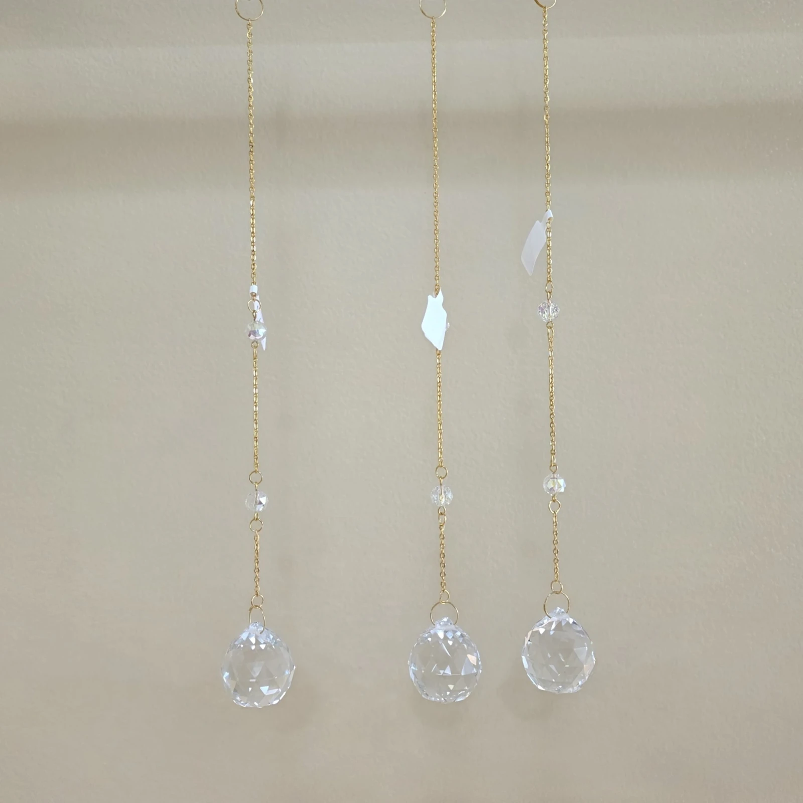 Three hanging crystal sun catchers with gold chains and beaded accents.