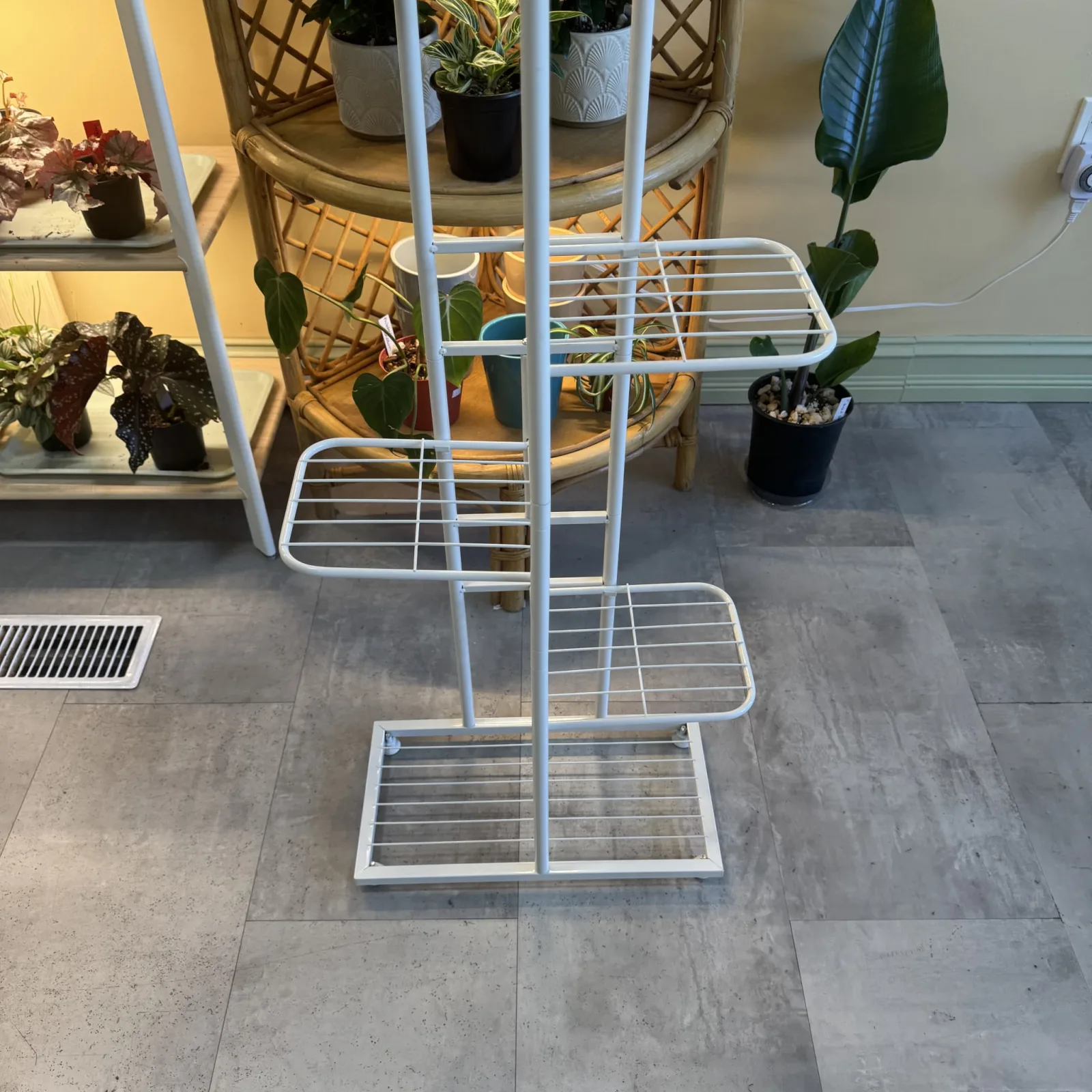 White metal plant stand with multiple shelves holding potted houseplants indoors.